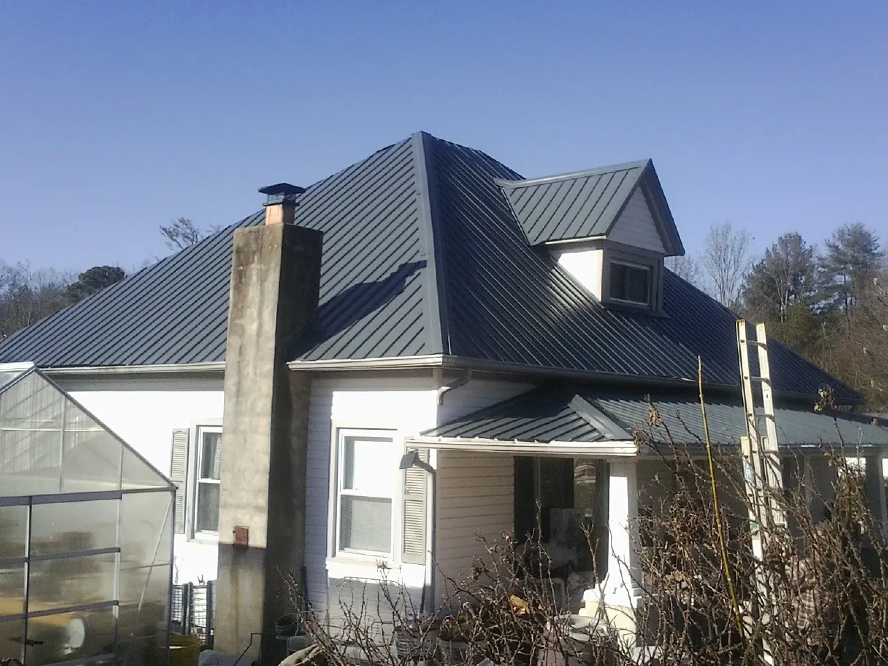 Dark blue standing seam metal roof on a white farmhouse with dormer — Slate & Tile Roof Repair by Roofing Brothers in River Grove