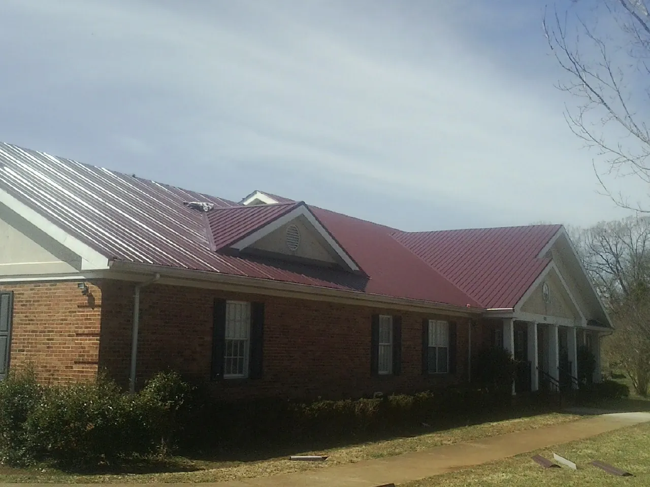 Red metal roof with gabled entries on a long brick building, from a Hail Damage Roof Repair job in River Grove