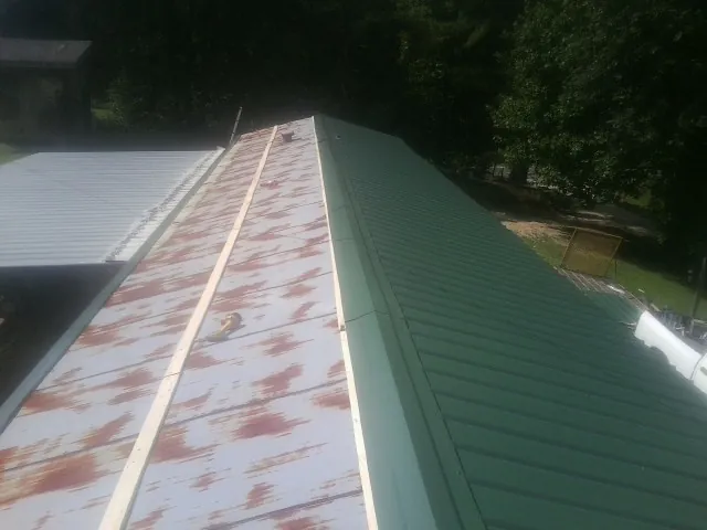 Old rusted panels beside newly installed green metal roofing in River Grove