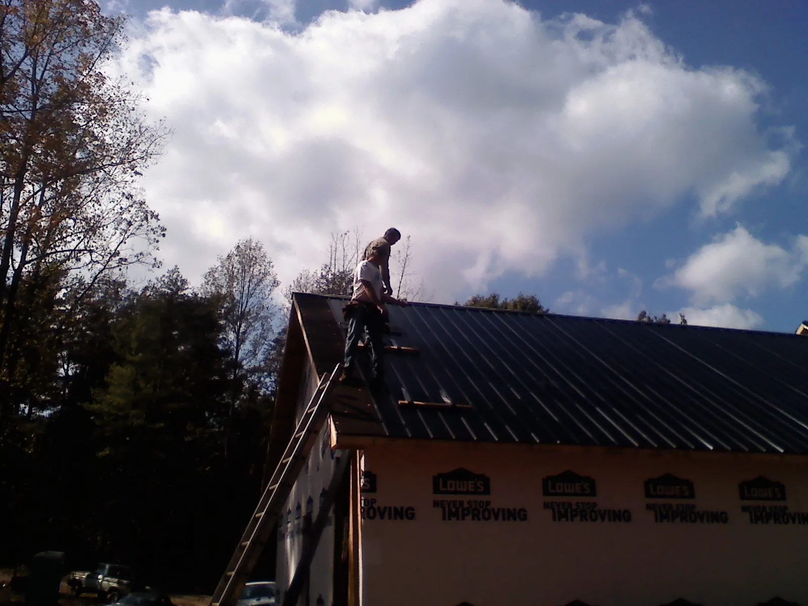 Roofer fastening dark metal panels high against a cloudy sky, from a Roof Inspection job in River Grove