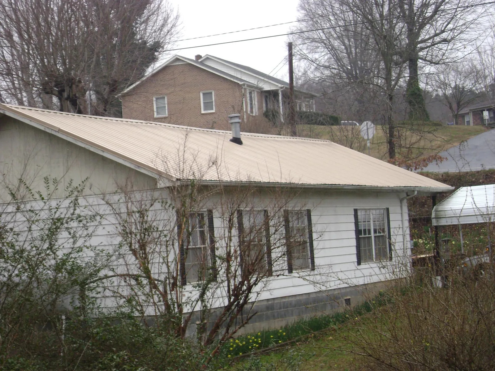 Tan metal roof on a white sided house set into a hillside — Commercial Roofing by Roofing Brothers in River Grove